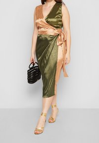 Robe portefeuille en satin vert et or rose avec texture léopard, dotée d'un décolleté en V profond et d'une ceinture à la taille. Assortie à un sac noir et des sandales dorées.
