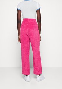 Pantalones de corduroy rosa de talle alto con un diseño de pierna recta, que cuentan con una superficie texturizada y bolsillos, combinados con zapatillas blancas.