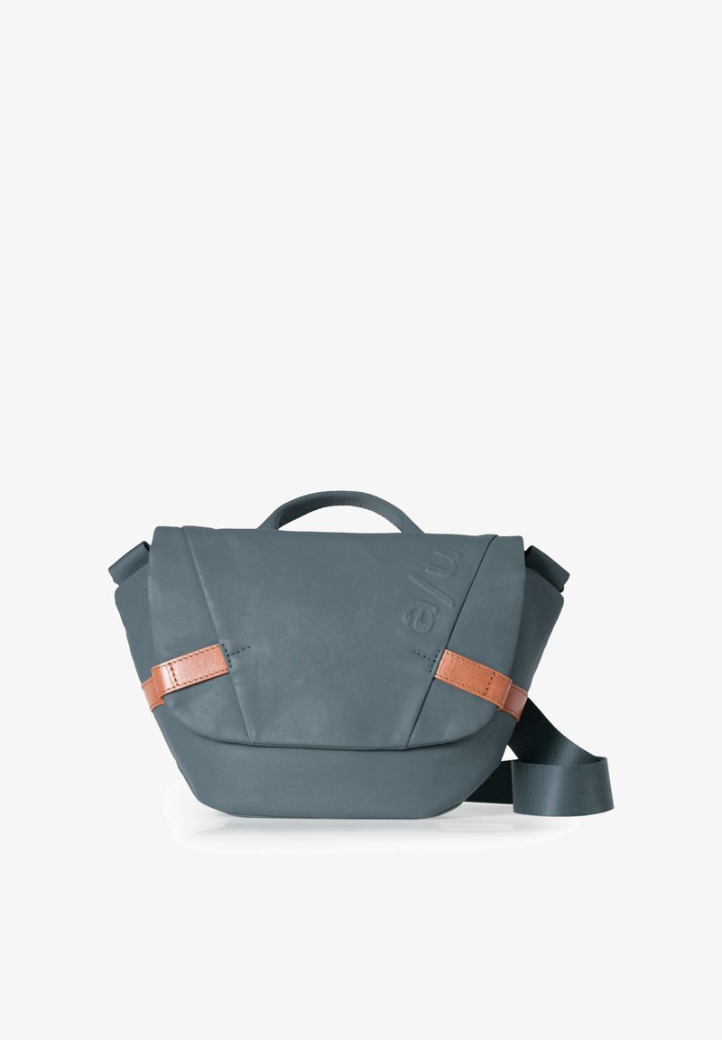 Kompakte dunkelgraue Umhängetasche mit hellbraunen Ledergriffen, einem oberen Tragegriff und einem breiten, verstellbaren Schulterriemen.