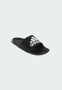 Černé sandály na klínu vyrobené z syntetického materiálu, s širokým popruhem s bílým logem Adidas, plochou podrážkou a hladkým povrchem.