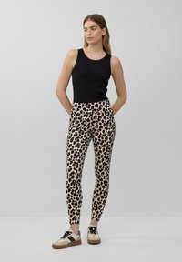 Czarny top na ramiączkach, dopasowane legginsy w cętki i trampki z beżową podeszwą i czarnymi akcentami. Gładka faktura i bezszwowy design.