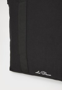 Crna torba s teksturiranom tkaninom, bočnim webbing detaljem i izvezenim logotipom u bijeloj boji na donjem rubu.