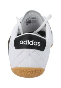 Vit sportskor med svart accent, med en quiltad textur på hälen och en texturerad gummisula, märkt "adidas" på baksidan.