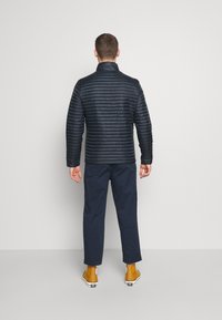 Quiltad marinblå jacka med hög krage, med horisontella linjer, kombinerad med marinblå byxor och senapsgula stövlar.