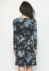Schwarzes Kleid mit floralem Muster in Blau und Creme, langen Ärmeln, tailliertem Schnitt und ausgestelltem Rock. Weicher, dehnbarer Stoff.