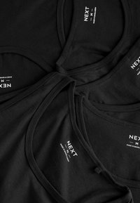 Sorte bomuldstanke med rund halsudskæring og smalle stropper. Hver skjorte har en hvid "NEXT"-label og en glat tekstur.