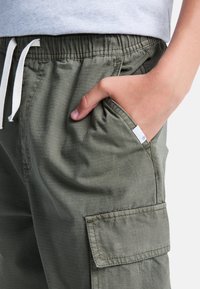 Olivengrüne Cargo-Shorts mit elastischem Bund, Kordelzugverschluss, Seitentasche und strukturiertem Stoff mit subtilen Rautenmuster.