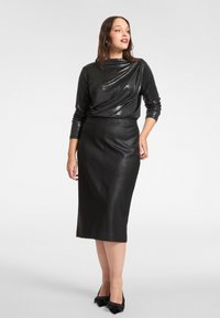 Czarna skórzana spódnica o dopasowanym kroju, zestawiona z ciemną, błyszczącą bluzką z długim rękawem. Obuwie to czarne buty z ozdobą w formie kokardy.