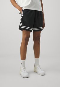 Black athletic shorts with white side stripes, featuring a comfortable fit and soft fabric. Worn with white sneakers and crew-length socks.