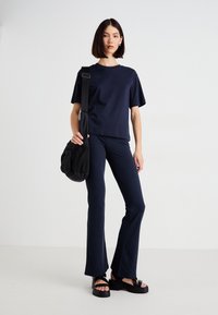 Una donna è in piedi indossando una maglietta blu navy e pantaloni a zampa d'elefante, sandali neri con platform e portando una borsa a tracolla nera.