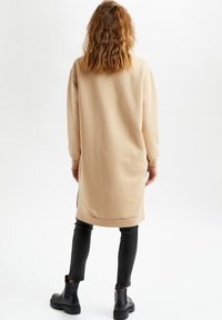 Beige sweatshirtklänning med långa ärmar, ribbade muddar och nederkant; sidofickor; matchad med svarta läderleggings och kraftiga svarta stövlar.