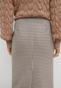 Pull en tricot marron avec un motif texturé, associé à une jupe crayon à carreaux arborant un design en pied-de-poule en noir, blanc et beige.
