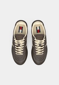 Σκούρα καφέ αθλητικά παπούτσια με κρέμ κορδόνια και επένδυση. Διαθέτουν καμπυλωτή ραφή και λαστιχένια σόλα. Η γλώσσα φέρει λογότυπο με κόκκινες, λευκές και μπλε ρίγες.