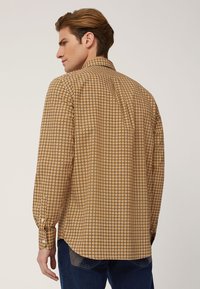 Camicia a maniche lunghe con bottoni di colore giallo con un piccolo motivo geometrico. Presenta un colletto, polsini con bottoni e un orlo arrotondato.