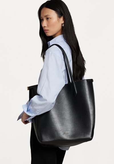 Μαύρη δερμάτινη τσάντα tote με στρογγυλεμένες πλευρές και δύο μακριές λαβές. Περιλαμβάνει ένα διακριτικό λογότυπο και μια λεία υφή χωρίς ορατά σχέδια.