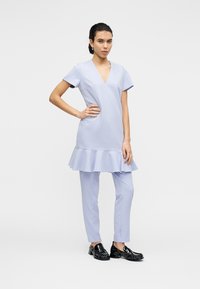 Φόρεμα μήκους μέχρι το γόνατο σε μωβ χρώμα με κοντά μανίκια και φαρδιά ποδιά, σε συνδυασμό με εφαρμοστά μωβ παντελόνια. Μαύρα παπούτσια χωρίς κορδόνια ολοκληρώνουν το σύνολο.