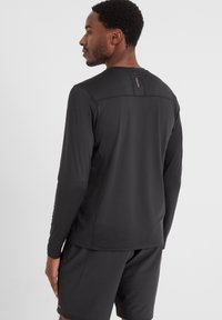 Black long-sleeve athletic shirt made from lightweight, stretchy material with a seamless back design and subtle logo detail at the neckline.