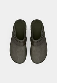 Sandales grises à enfiler avec une texture semblable au daim, ornées d'une bande sombre sur le dessus et d'un détail de bouton circulaire sur le côté.