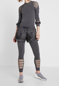 Grått träningsset som består av en långärmad topp med nätinslag, mönstrade shorts och leggings med utskärningar. Gråa slipskor.