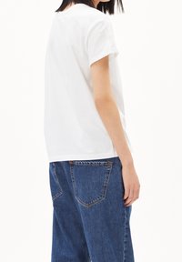 Camiseta de algodón blanca con mangas enrolladas y cuello redondo, combinada con jeans de mezclilla azules de cintura alta que presentan bolsillos traseros visibles.