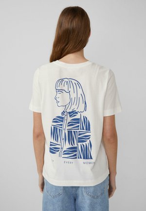 T-shirt en coton crème avec une illustration bleue représentant un profil de personne portant une chemise à motif texturé, avec le texte en dessous : "CHAQUE INSTANT."