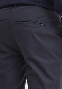 Marineblaue Hose aus Baumwolle mit glatter Textur, ausgestattet mit zwei Gesäßtaschen und einem kleinen Markenetikett an der rechten Tasche.