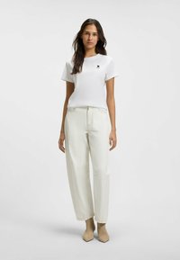 White short-sleeve t-shirt with a small black heart design, paired with high-waisted cream trousers and beige pointed-toe ankle boots.