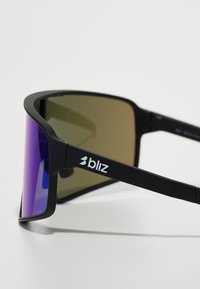 Lunettes de sport noires avec de grandes lentilles teintées en violet et un dégradé bronze, arborant un logo sur la branche et une monture en plastique robuste.