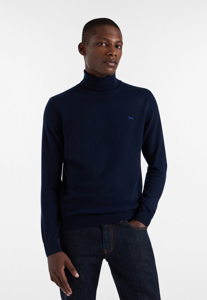 Mornarsko moder pulover z visokim ovratnikom, izdelan iz mehkega materiala, z majhnim svetlomodrim logotipom na prsih ter rebrastimi manšetami in robom.