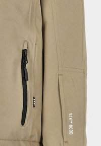 Beige Außenjacke mit einem Reißverschlussfach, strukturiertem Stoff und bedrucktem Logodetail "STX™ 8000" in der Nähe des Bündchens.