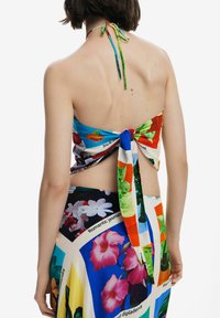 Top a halter multicolore con stampa floreale tropicale, realizzato in tessuto leggero. Si annoda sul retro a fiocco, mostrando la pelle e la zona delle spalle.