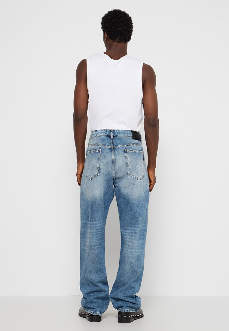 Jean en denim bleu clair à coupe décontractée, avec un délavage usé, des poches arrière et un patch en cuir à la taille.