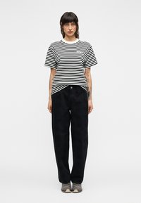 Μαύρο και άσπρο ριγέ κοντομάνικο μπλουζάκι σε συνδυασμό με φαρδιά, μαύρη παντελόνα. Τα παπούτσια έχουν απαλό γκρι σχέδιο.