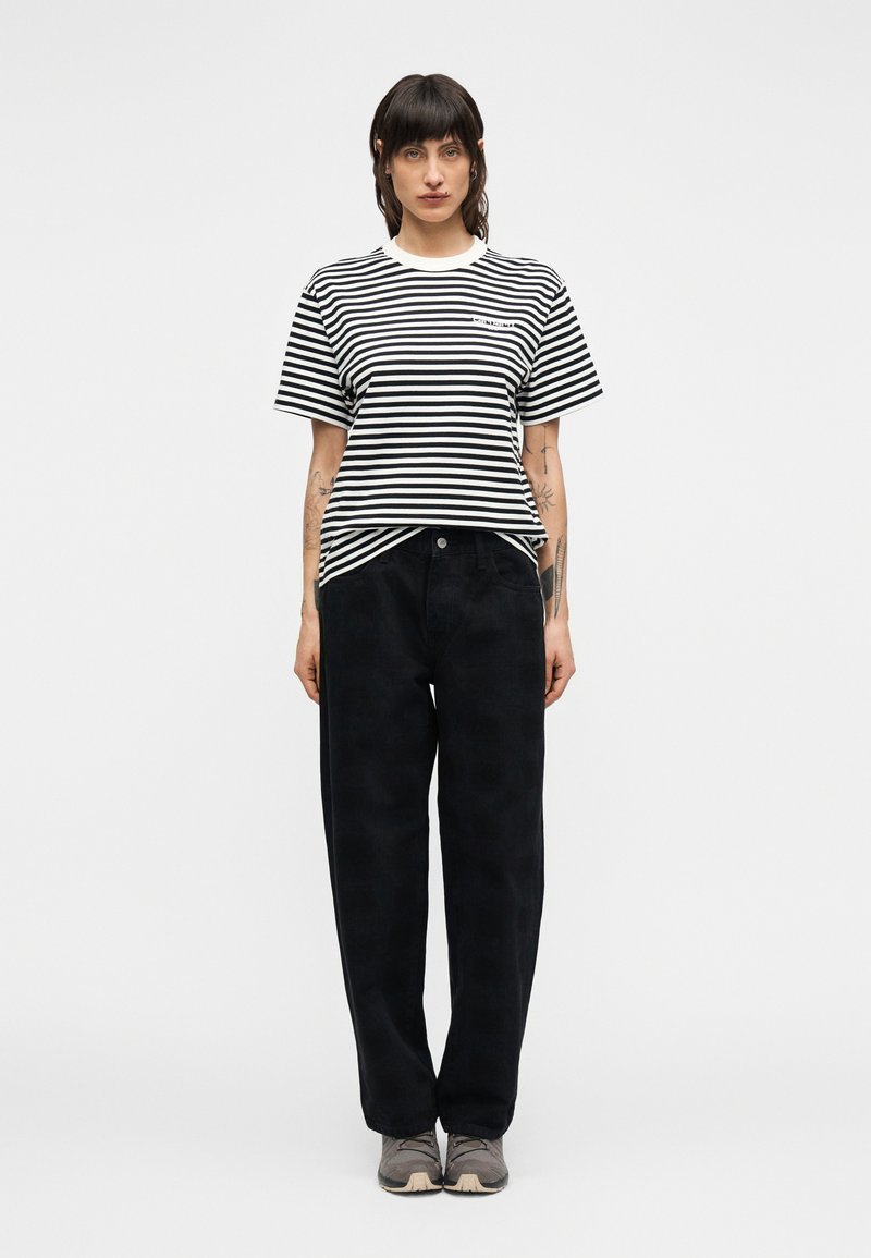 Maglietta a maniche corte a righe bianche e nere abbinata a pantaloni neri larghi. Le calzature presentano un design grigio tenue.