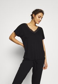 Black loungewear set featuring a short-sleeved top with a lace-trimmed V-neck and drawstring waist pants, made of soft fabric.