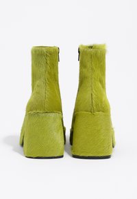 Botas de tobillo de pelo sintético verde con una plataforma gruesa y tacón alto. Presentan una cremallera en la parte posterior y una textura suave.