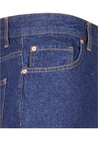 Jeans de mezclilla azul oscuro con una cintura de altura media, remaches de cobre y costuras naranjas. Incluye un pequeño bolsillo delantero y bolsillos traseros.