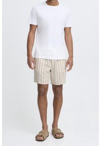 T-shirt en coton blanc associé à un short beige à rayures ; le short présente des rayures horizontales, un tissu texturé et une coupe décontractée. Des sandales brunes complètent le look.
