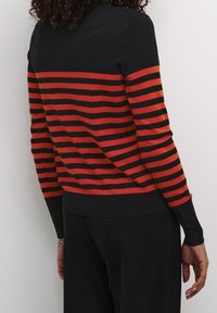 suéter rayado en negro y rojo con un cuello alto, mangas largas y puños acanalados. Las rayas alternan en ancho. Material de punto texturizado.