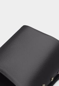 Καπάκι μαύρης δερμάτινης τσάντας με ομαλή υφή και τρεις στρογγυλές ασημένιες τρούκ κατά μήκος της άκρης σε φωτεινό φόντο.