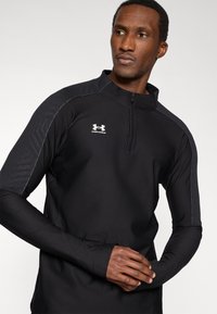 Μαύρη αθλητική μπλούζα με μακριά μανίκια και φερμουάρ στο ένα τέταρτο, με υφασμένους τόνους στους ώμους και κεντημένο λευκό λογότυπο μπροστά. Λείο, εφαρμοστό σχέδιο.