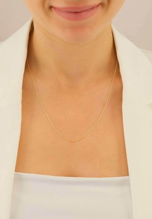 Collier en or avec un design délicat, une texture lisse et une brillance subtile, porté sur un haut blanc avec un blazer.
