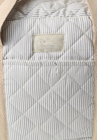 Τσέπη από καπιτονέ ύφασμα σε ανοιχτό μπλε και λευκές ρίγες, με ετικέτα που απεικονίζει ένα σύννεφο και το κείμενο «Cam Cam Copenhaghen».