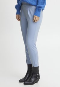 Hellblaue, maßgeschneiderte Hosen mit glatter Textur und Bundfalten, kombiniert mit schwarzen, ankle boots mit Absatz, die eine Riemendetail aufweisen.