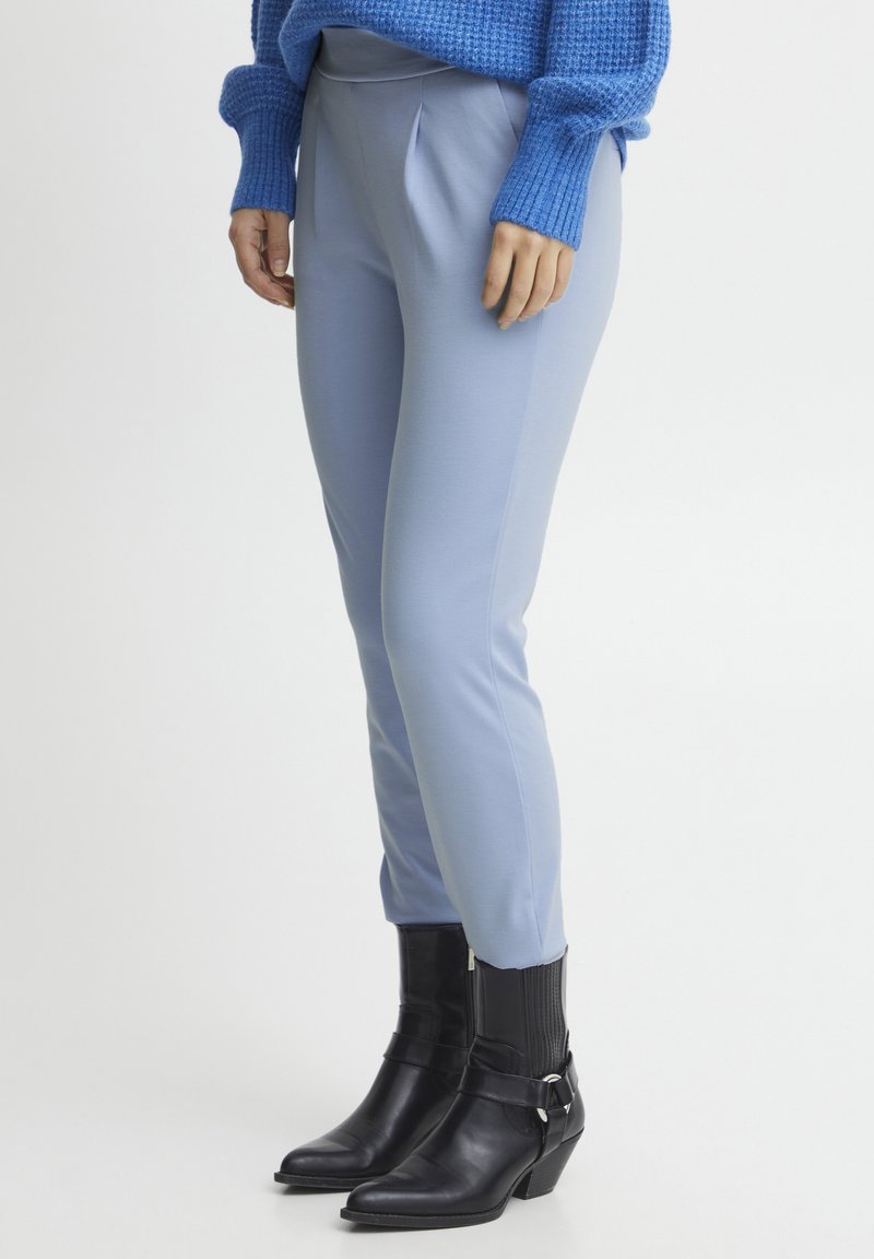 Hellblaue, maßgeschneiderte Hosen mit glatter Textur und Bundfalten, kombiniert mit schwarzen, ankle boots mit Absatz, die eine Riemendetail aufweisen.