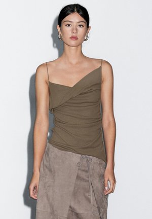 Haut ajusté vert olive avec un design drapé, décolleté asymétrique et fines bretelles, associé à une jupe en suède grise avec des liens.