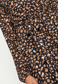 Vestido de tela negra con un patrón de manchas marrones y blancas. Incluye una cintura ajustada con cinturón y puños fruncidos. Textura suave.