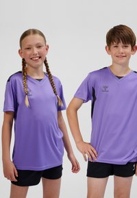 Lila träningsskjortor med korta ärmar, svarta detaljer på axlarna och V-ringning, kombinerade med svarta shorts. Mjuk tygstruktur.