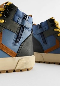 Wysokie sneakersy w kolorze niebieskim z szarymi, brązowymi i czarnymi akcentami. Posiadają teksturowany kanwas, dekoracyjne zamki błyskawiczne oraz gumowe podeszwy z wzorem antypoślizgowym.