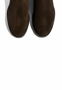 Botas de tobillo de ante marrón con una textura suave y punta redonda. Diseño con doblez y sutil detalle de costura, con una estética elegante y minimalista.